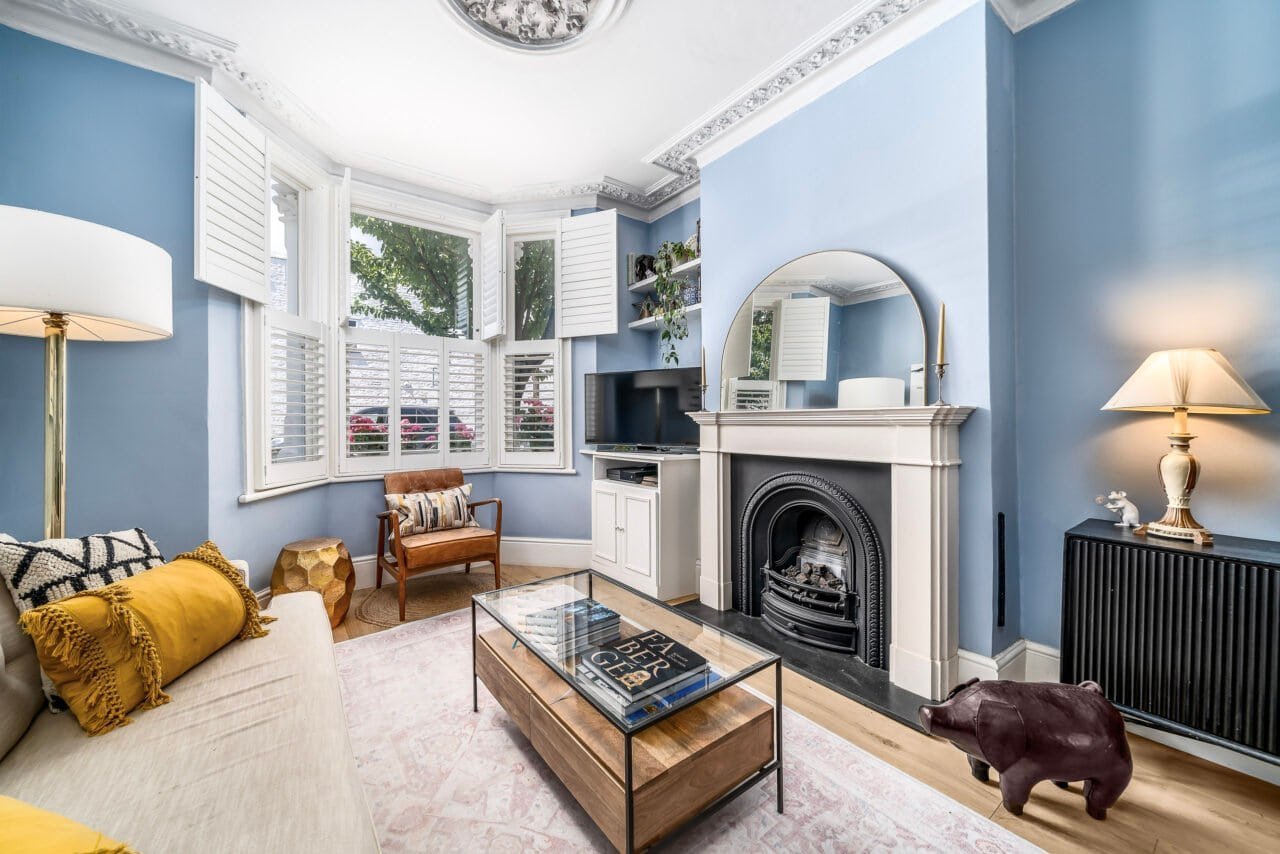 A colourful living room with blue walls, fireplace, and large bay windows.