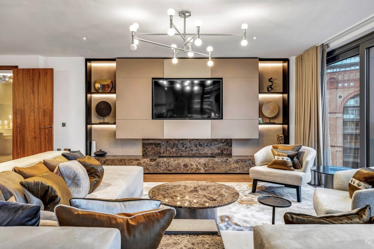 Modern living room with beige walls, large TV, and stylish furniture, bright natural light.