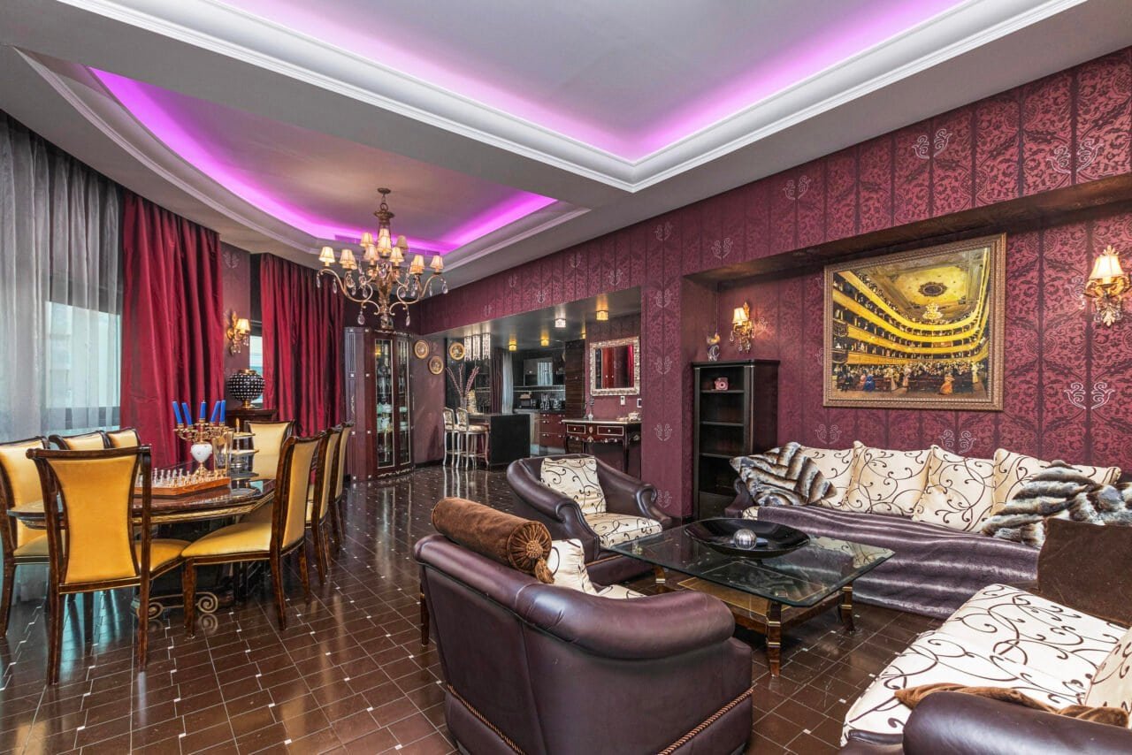 Luxurious living room with elegant furniture, chandelier, and vibrant pink lighting.