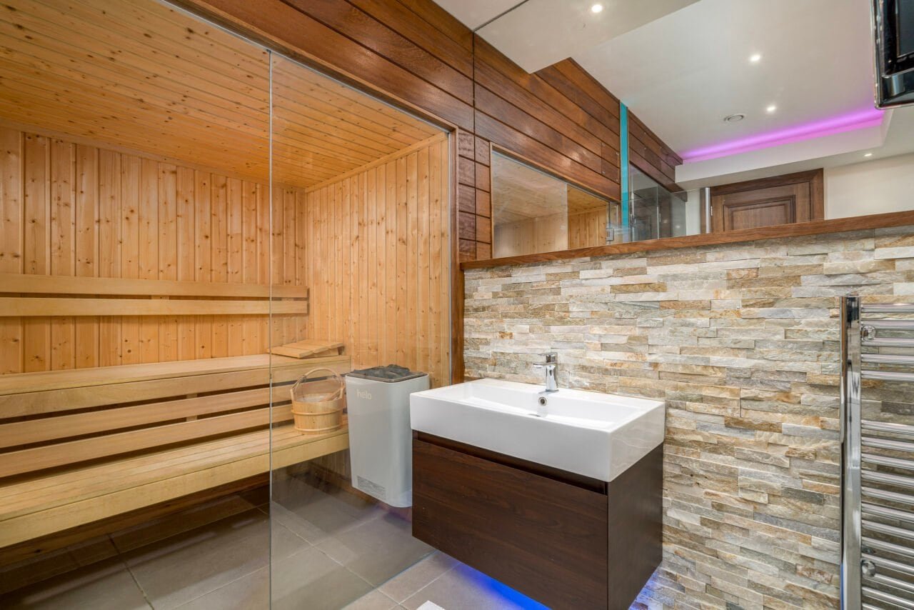 A sauna room with wooden benches and a modern washbasin area in a wellness centre.