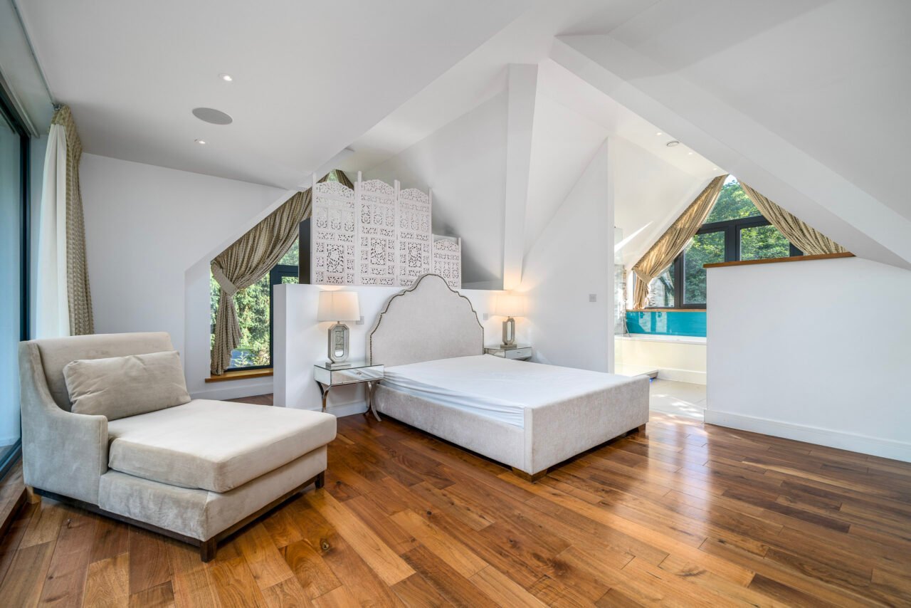 Spacious modern bedroom with white walls, wooden flooring, and large windows.
