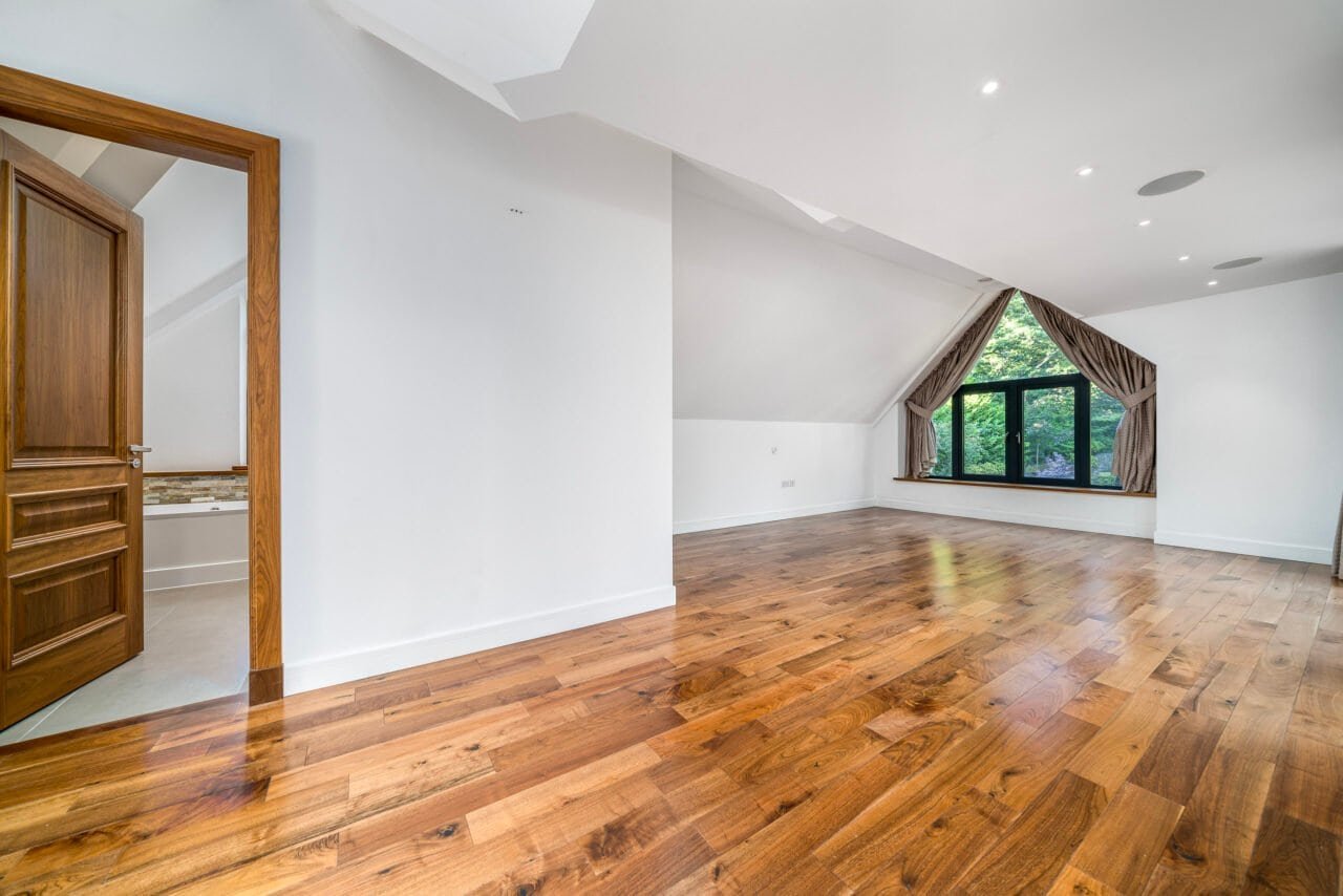 Spacious empty room with wooden flooring and large window in modern home.
