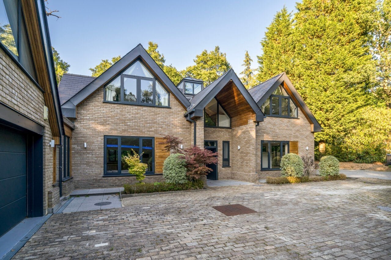 Modern brick house with large glass windows and landscaped garden in a wooded area.
