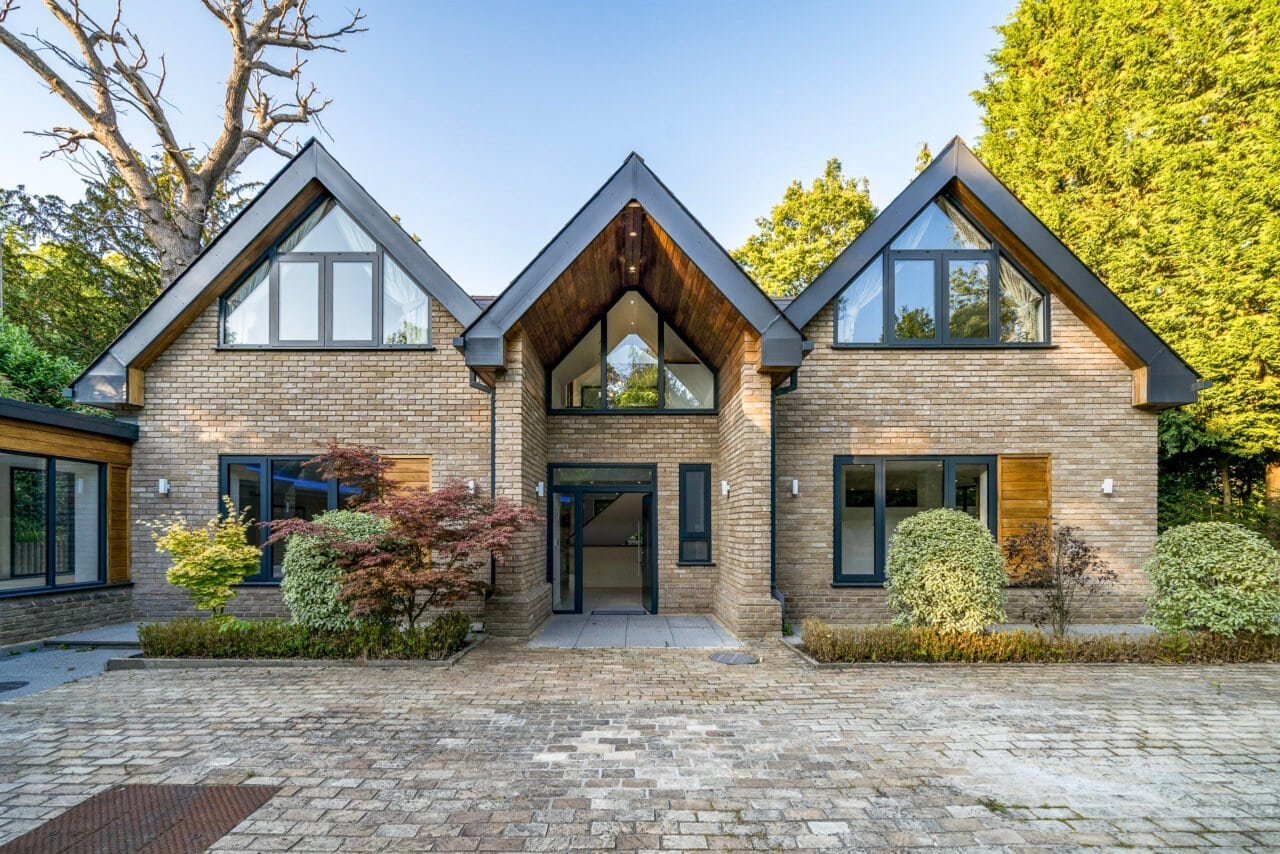 Modern detached house with brick facade and large windows in a lush green setting.