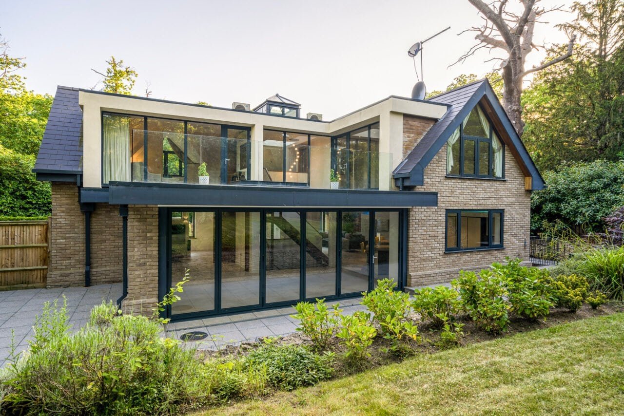 Modern two-storey house with large glass windows and garden in a lush green setting.