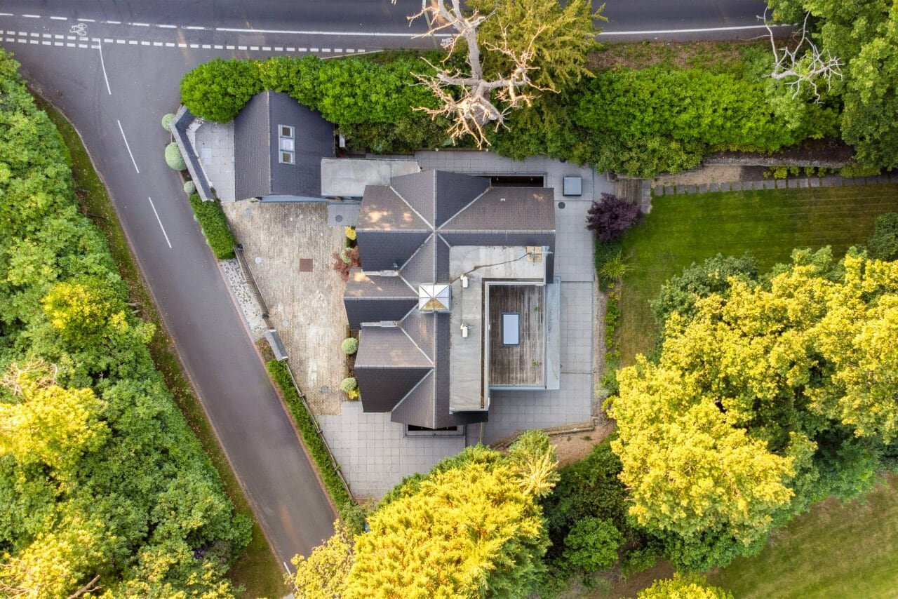 Aerial view of a modern house surrounded by lush greenery and trees in a residential area.