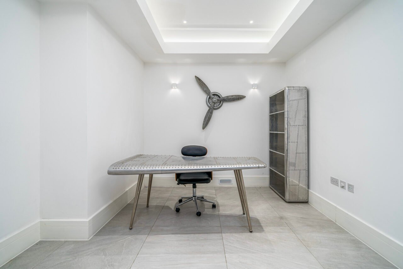 A modern, minimalist home office with white walls, a desk, and a ceiling fan.