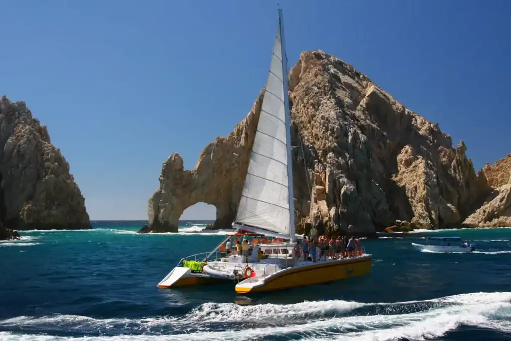Is Cabo San Lucas Safe In 2025? What Puerto Los Cabos Visitors And Homeowners Should Know – Homes For Sale In Plc Sailboat Navigating Near Rocky Cliffs At Puerto Los Cabos With Clear Blue Skies In The Background,