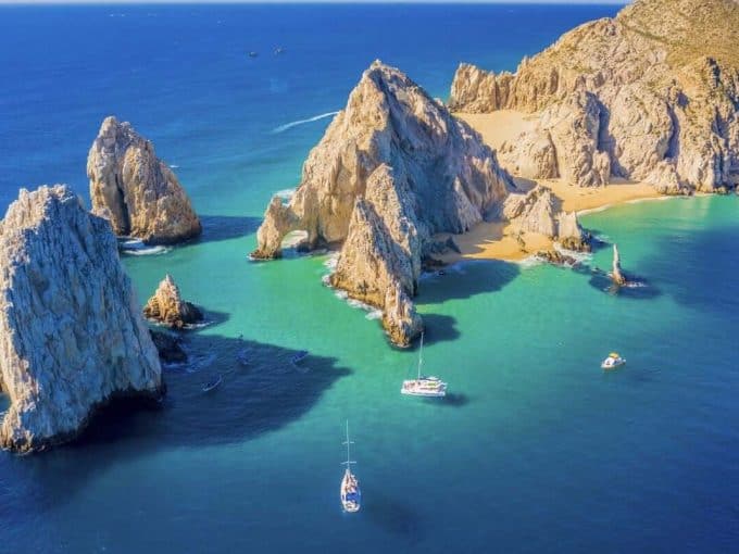 Stunning Aerial View Of Puerto Los Cabos Featuring Rocky Cliffs, Turquoise Waters, And Yachts, Highlighting The Luxurious Coastal Real Estate Opportunities In Puerto Los Cabos.