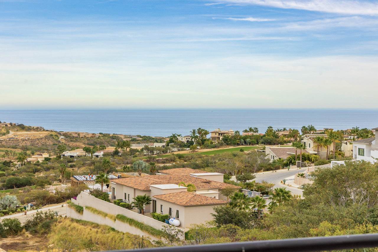 Breathtaking View Of Puerto Los Cabos Real Estate With Lush Greenery, Residential Homes, And Panoramic Ocean Horizon In The Background.