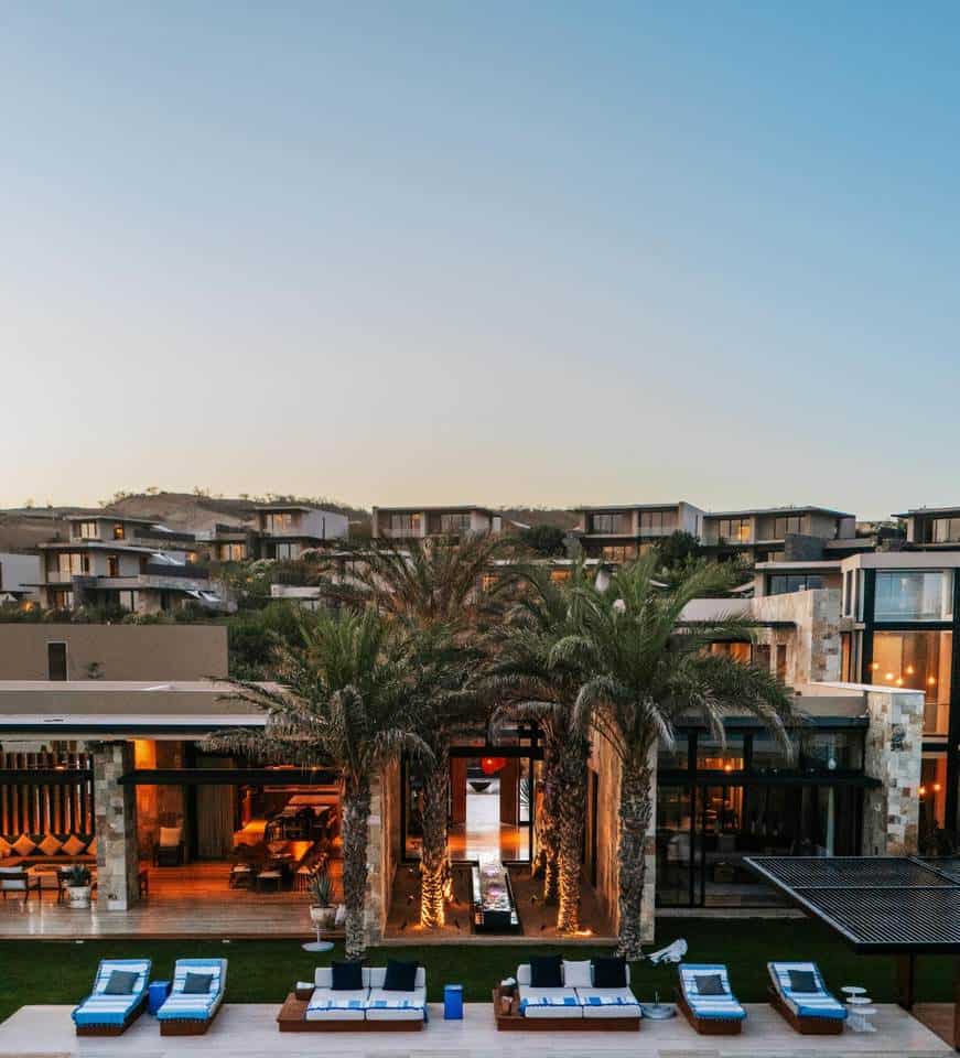 Puerto Los Cabos Luxury Residential Community With Modern Architecture, Lush Palm Trees, And An Inviting Outdoor Lounge Area At Sunset.