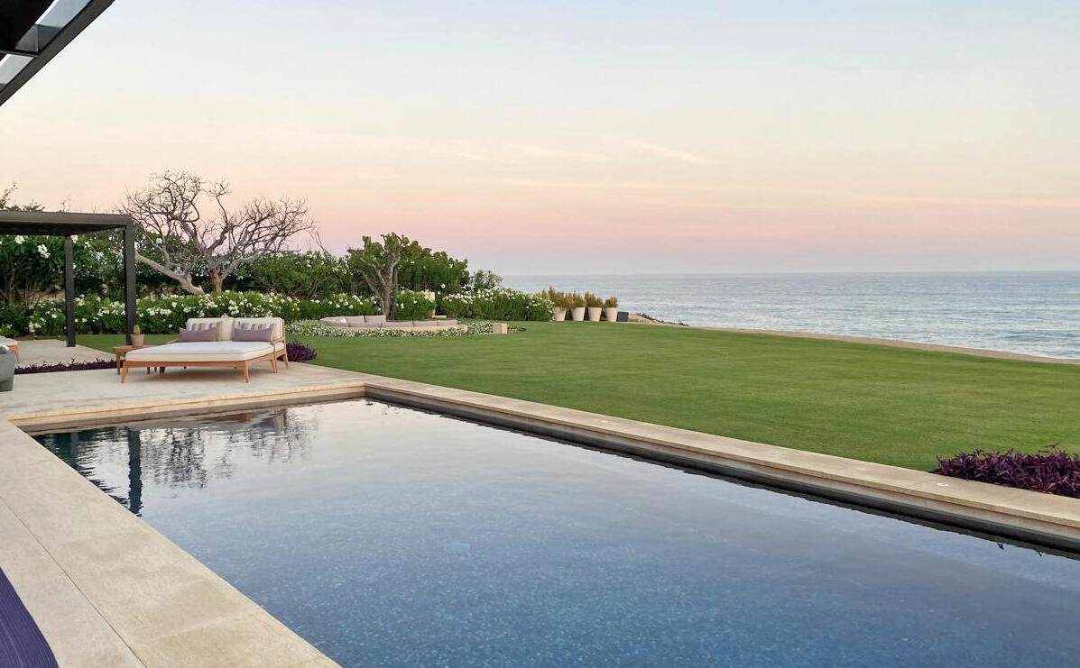 1. Beautiful View Of Puerto Los Cabos Coastline With A Modern Infinity Pool, Lush Greenery, And Sunset Sky, Ideal For Luxury Real Estate In Puerto Los Cabos.