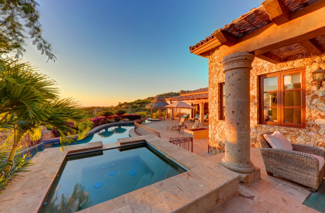 Home – Homes For Sale In Querencia Warm-Toned Stone Villa At Sunset Featuring A Private Spa, Curved Pool, Palapa, And Lush Tropical Landscaping In Querencia Real Estate, San José Del Cabo.