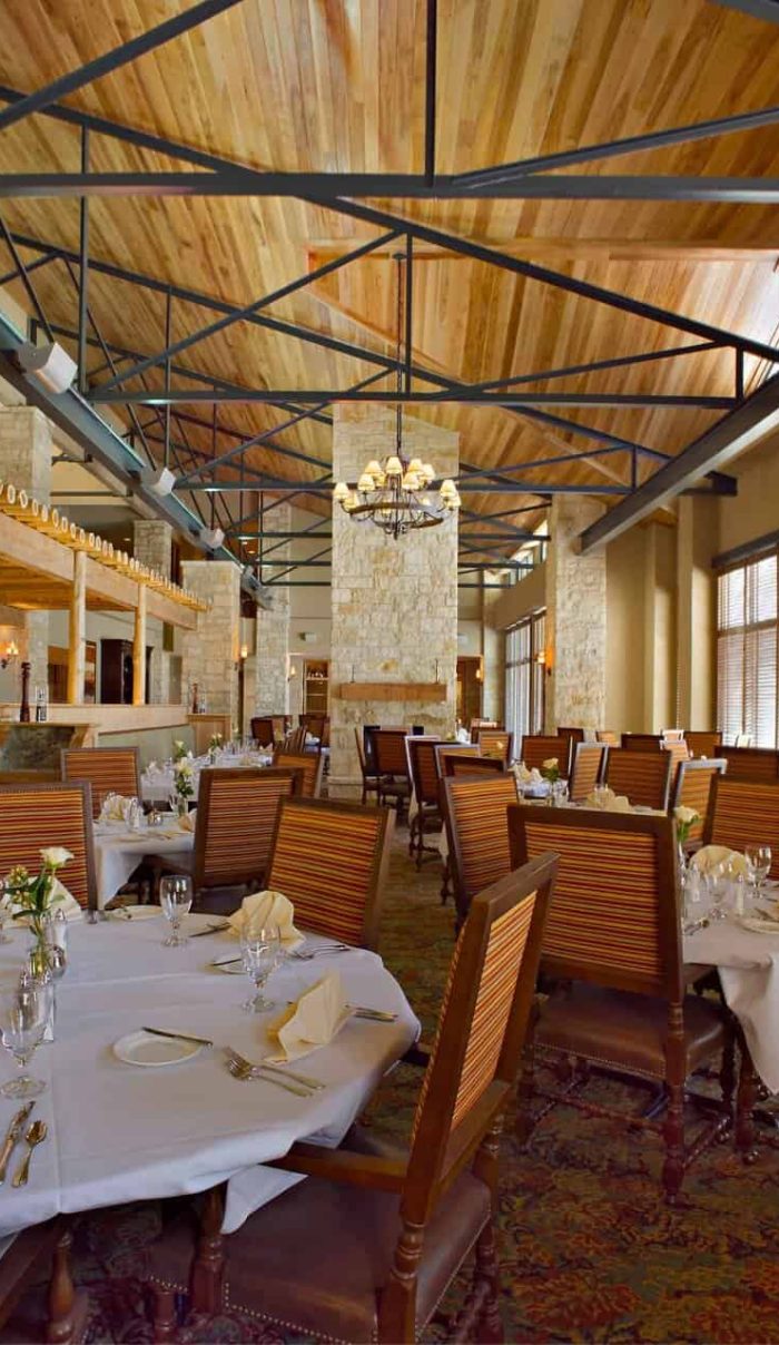Elegant Interior Of A Querencia Real Estate Restaurant Featuring Stone Walls, High Wooden Ceilings With Exposed Beams, And Beautifully Set Dining Tables For A Refined Dining Experience.