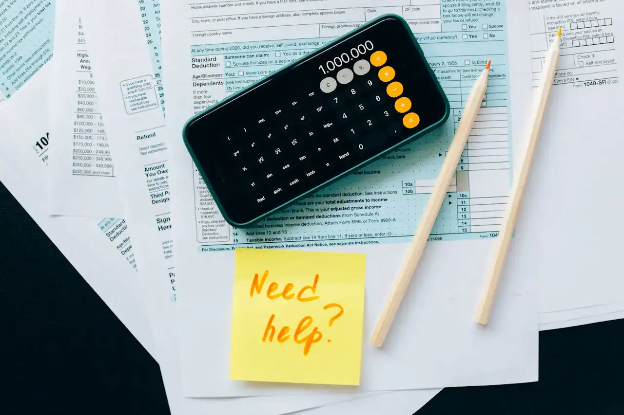 A imagem mostra um celular aberto na calculadora, papéis de documentos, talvez recibos ou formulários, sugerindo atividades como cálculo de impostos, análise fiscal ou declaração