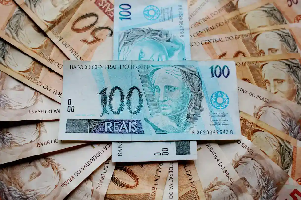 Imagem que apresenta várias cédulas de dinheiro; no centro, destacam-se duas notas de cem reais, cercadas por diversas notas de cinquenta reais.