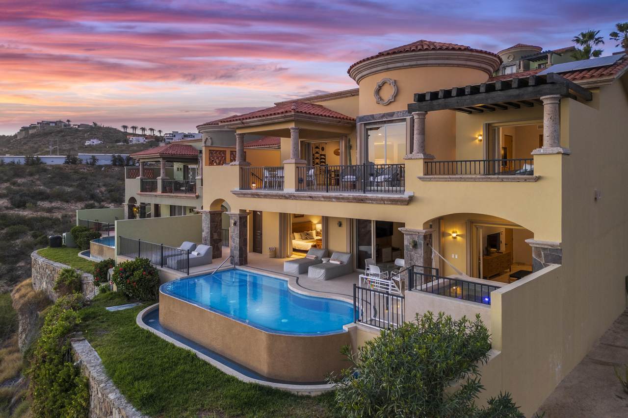 Elegant Multi-Level Villa With Terracotta Roof, Stone Columns, And A Cliffside Infinity Pool At Sunset In Quivira Real Estate, Cabo San Lucas.