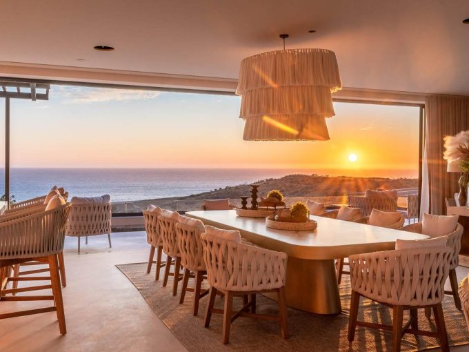 Elegant Open-Concept Dining Area With Woven Chairs, Pendant Lighting, And Panoramic Sunset Views Over The Pacific Ocean In Quivira Real Estate, Cabo San Lucas.