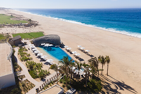 Aerial Shot Of The Modern Quivira Beach Club Pool, Palapa Roof, And Palm Trees, Set Directly On The Wide Sandy Beach.
