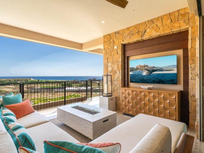 Stunning View From A Quivira Los Cabos Luxury Condo Balcony With Ocean And Golf Course Scenery, Comfortable Seating, And A Modern Living Room Featuring A Large Tv And Exquisite Stone Accents.