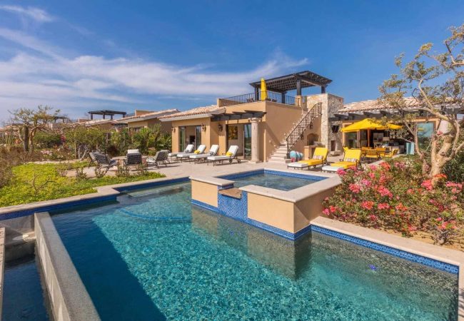 Luxurious Villa Exterior At Quivira Los Cabos Featuring A Private Pool And Outdoor Lounging Area, Set Against A Vibrant Clear Sky And Lush Desert Greenery.