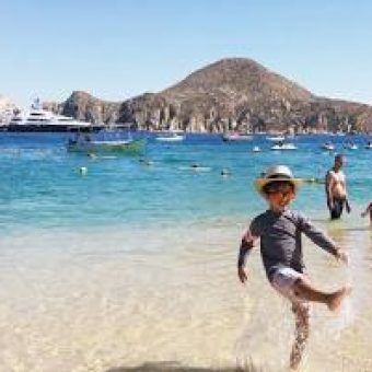 Kids Playing And Kicking Water In The Shallow Quivira Beach Area With Boats And Mountains In The Background.