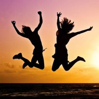 Silhouettes of two people jumping at sunset with ocean background.