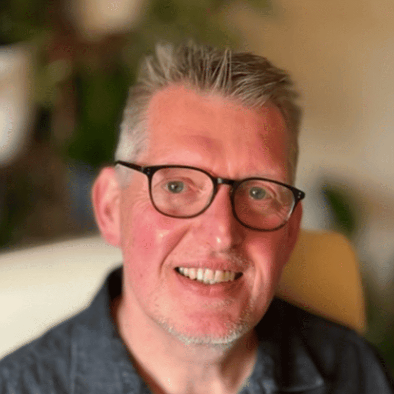 Close-up of a smiling man with glasses in a professional setting.