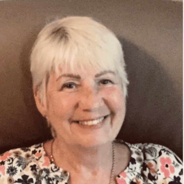 Smiling woman with short white hair and floral top at Raw Horizons.
