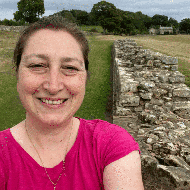 Woman smiling at ancient stone ruins in a lush green landscape.