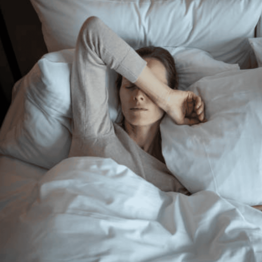 Woman resting peacefully in bed with eyes closed, relaxing in a cozy bedroom setting.