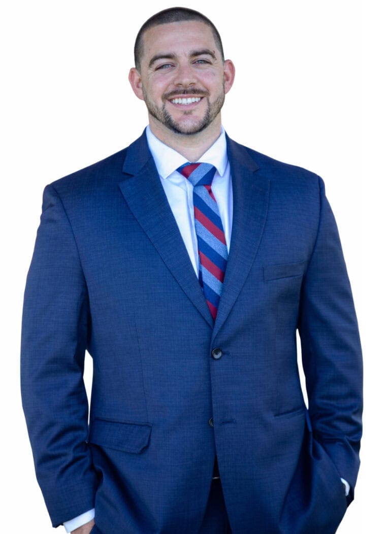 Garrett Mann wearing a blue suit and striped tie, smiling confidently.