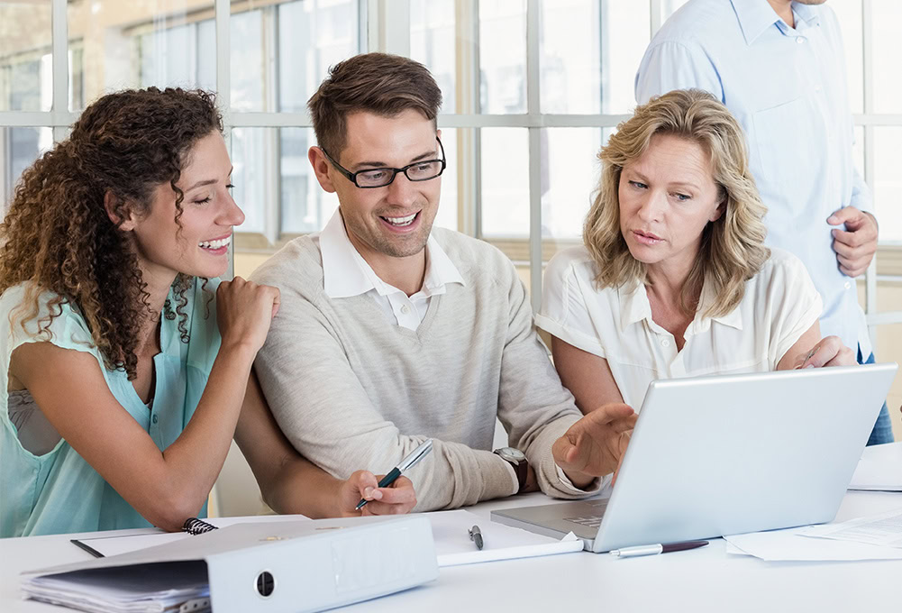 Businessman Working At Desk With Meeting In Background