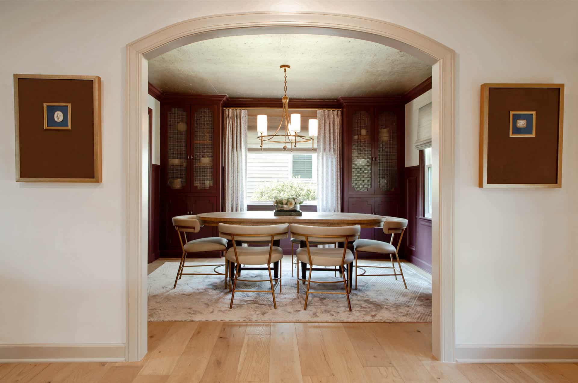 Kitchen with a wood island, upholstered stools, and light cabinets accented by gold hardware and decorative wall shelves.