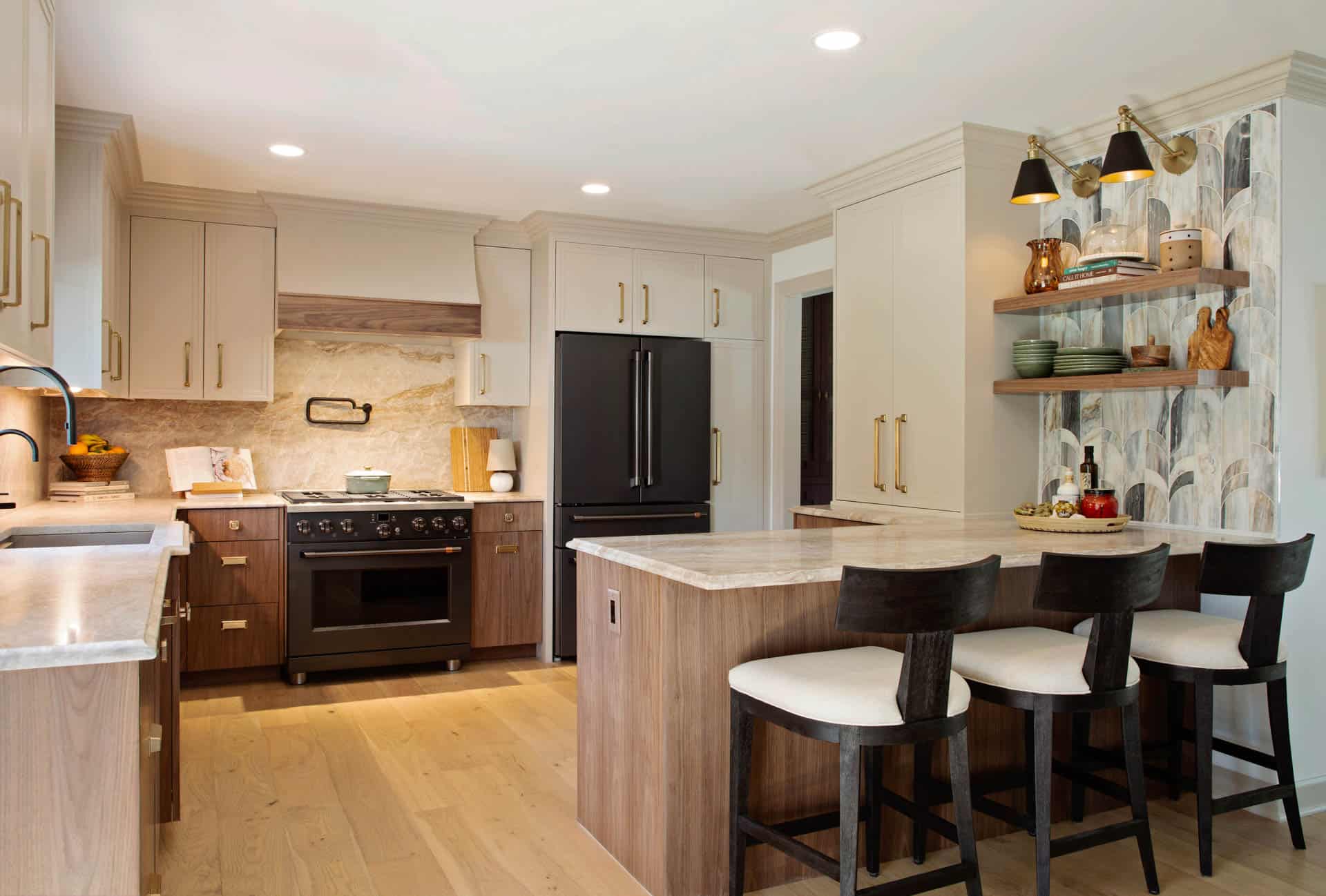 Kitchen with a wood island, upholstered stools, and light cabinets accented by gold hardware and decorative wall shelves.