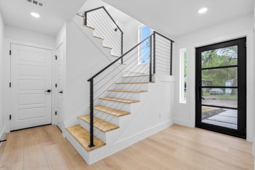 Minimalist entryway with black metal door, clean stairs and light natural-tone flooring