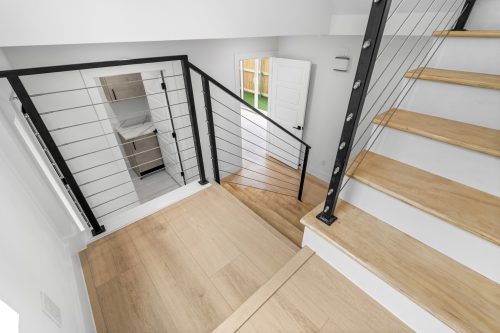 Contemporary staircase design with cable railings and pale wood-look composite flooring