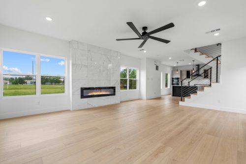 Open living room with linear fireplace, large windows, and light wood composite flooring in High Tide