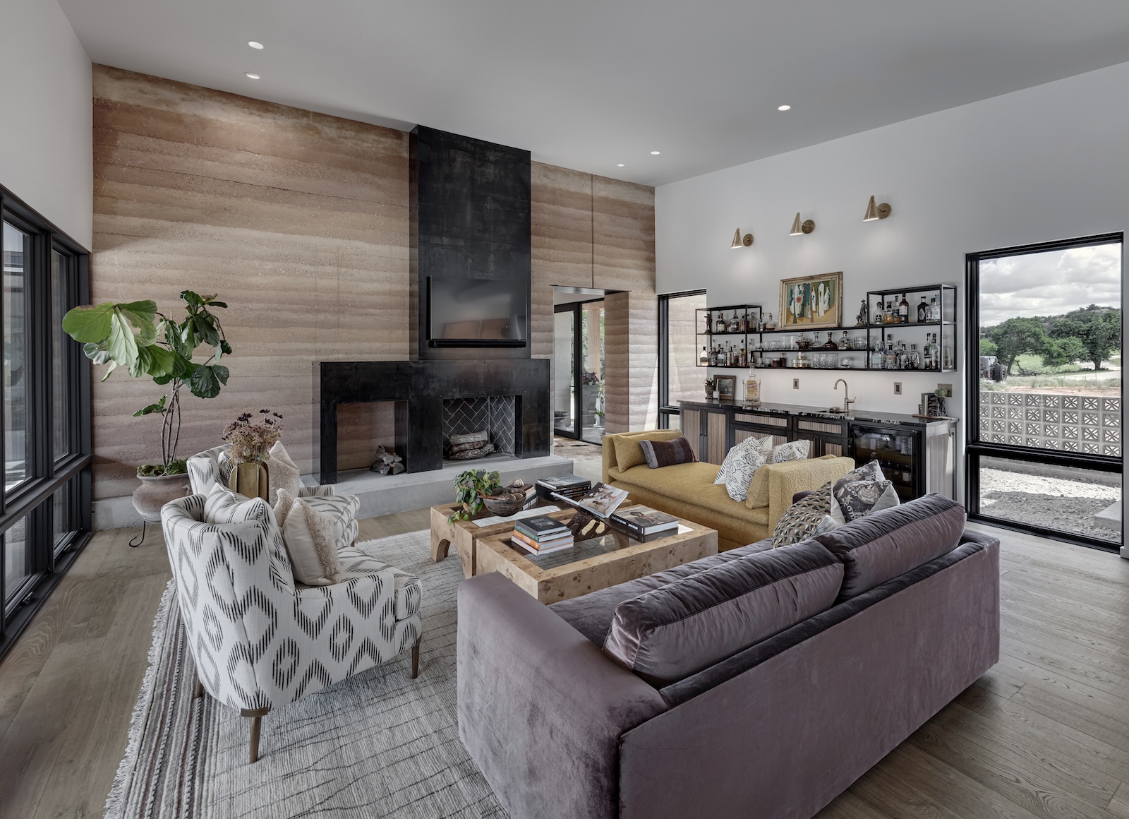 Open living space with real wood floors, warm neutral tones, and large windows framing outdoor views