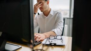 Frustrated man with glasses at desk, experiencing website issues.