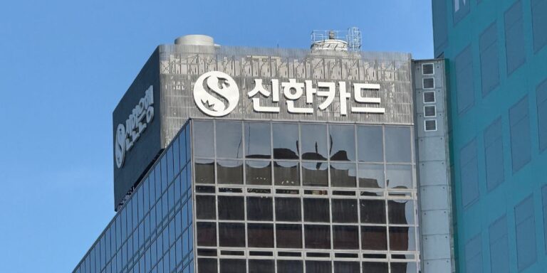 Glass office building with Shinhan Card sign and circular logo on the top, blue sky in background.