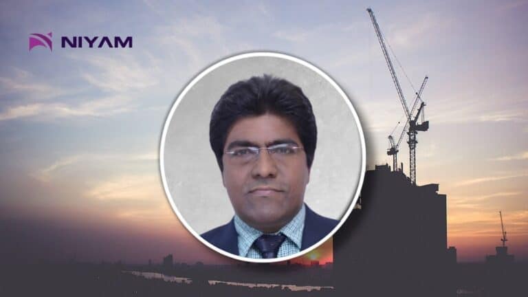 Portrait of a man in a suit with glasses, set in a circular frame over a construction site at sunset; NIYAM logo in the top-left.
