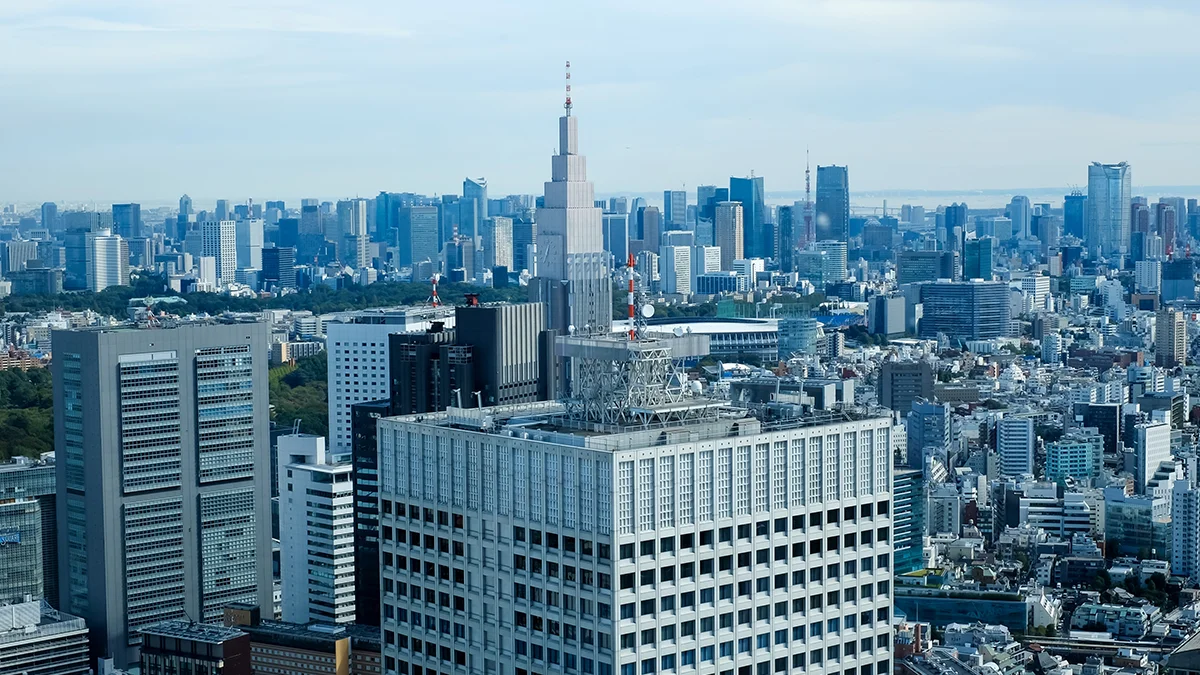 Aerial view of a dense city skyline with many high-rise buildings and a prominent stepped central tower against a blue sky.