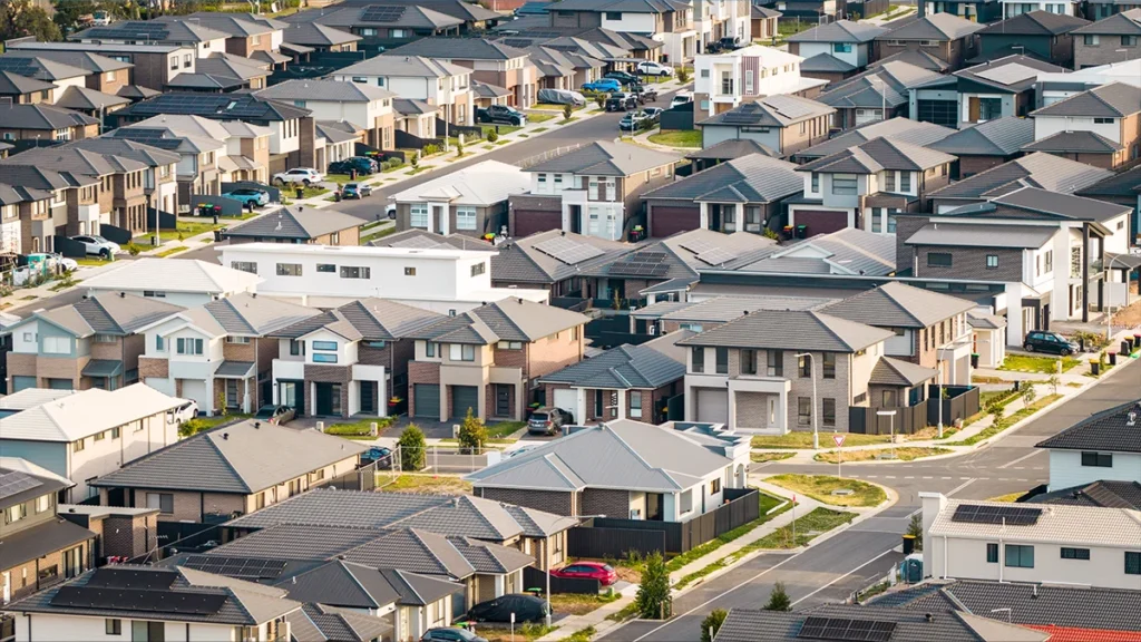 Aerial view of a dense suburban neighborhood with rows of modern two‑story houses and winding streets on a sunny day.