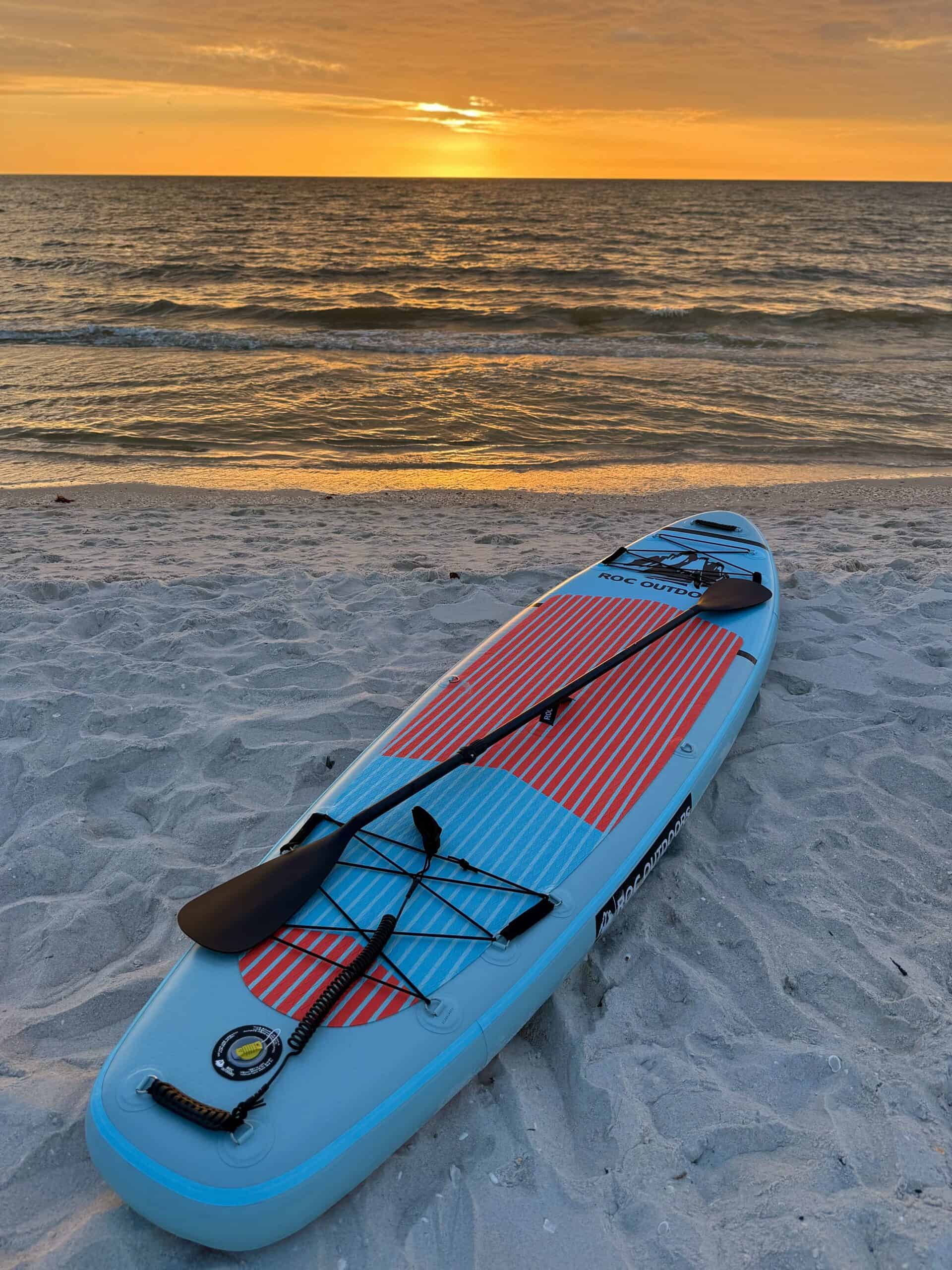 Colorful paddleboard on sandy beach with ocean and sunset backdrop, perfect for water recreation and beach day rentals.