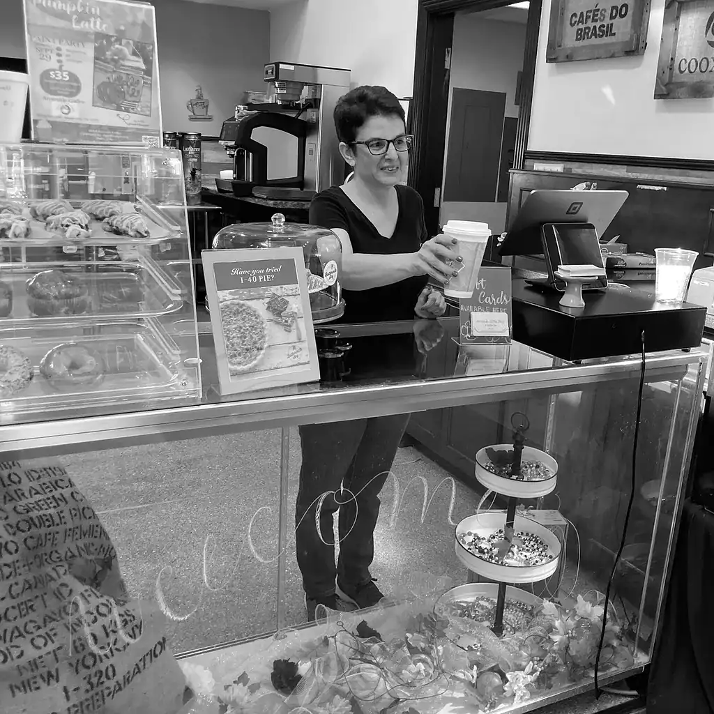 Meet the staff 2 Coffee shop counter with a barista serving a hot beverage, pastries on display, and a welcoming atmo.