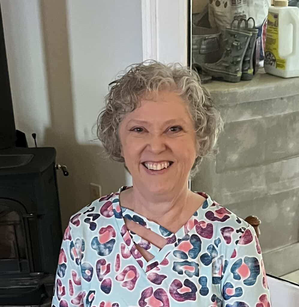 Meet the board 8 Smiling woman with curly gray hair sitting at a table, representing the board at Riverside Coffee Sh.