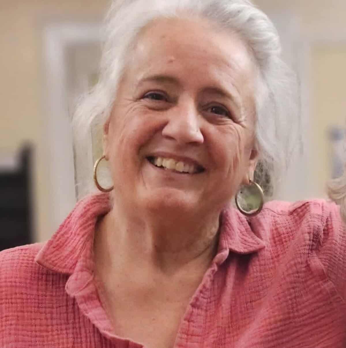 Meet the board 7 Smiling woman with white hair and pink shirt at Riverside Coffee Shop.