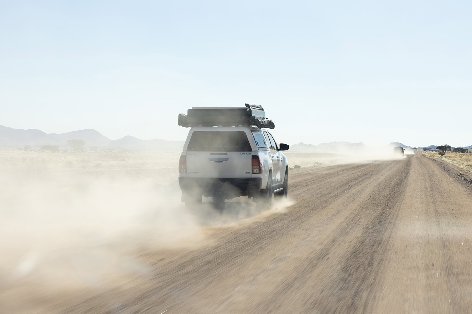 Dusty desert road with a white SUV showcasing stainless steel canopies in a rugged environment.