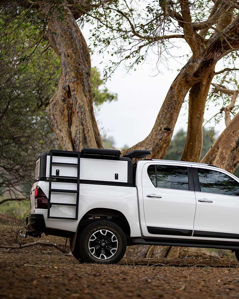 Heavy-duty stainless steel canopies installed on a white pickup truck in an outdoor, wooded setting for durability and outdoor utility.